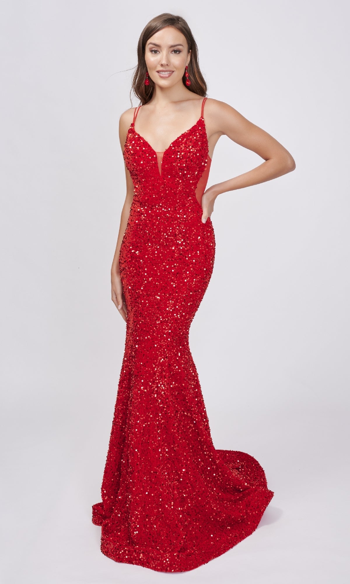 A woman poses against a white background in the Nina Canacci 4420 Long Formal Sequin Dress—a floor-length, fitted red gown featuring thin straps and a deep sheer v-neckline.